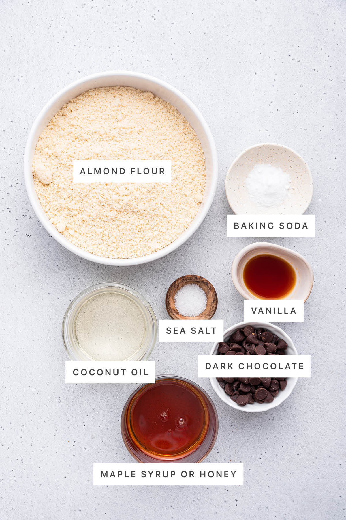 Ingredients measured out to make Almond Flour Chocolate Chip Cookies: almond flour, baking soda, sea salt, vanilla, coconut oil, dark chocolate and maple syrup/honey.