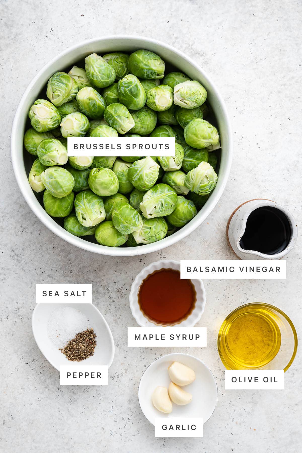 Ingredients measured out to make Balsamic Roasted Brussels Sprouts: brussels sprouts, balsamic vinegar, sea salt, pepper, maple syrup, garlic and olive oil.