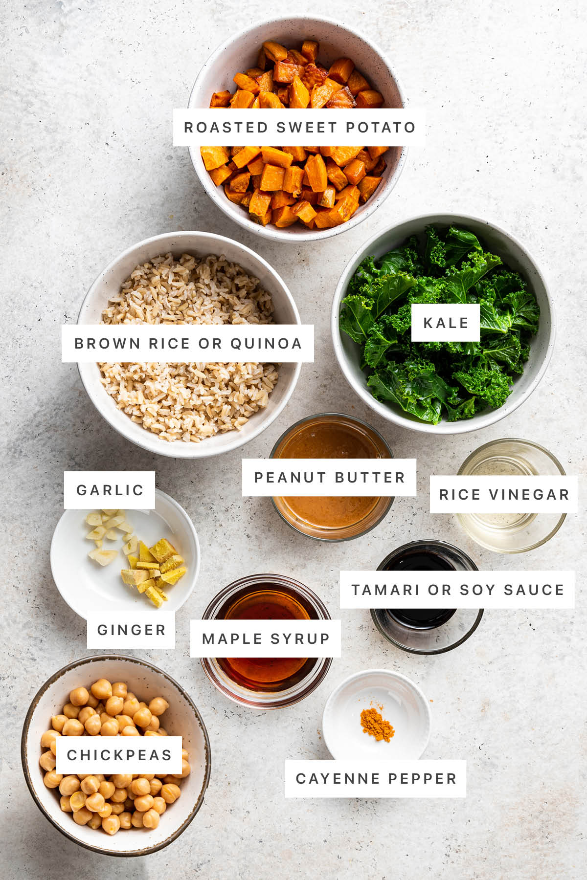 Ingredients measured out to make Kale and Sweet Potato Brown Rice Bowls: roasted sweet potato, brown rice, kale, garlic, ginger, peanut butter, rice vinegar, maple syrup, tamari, chickpeas and cayenne pepper.