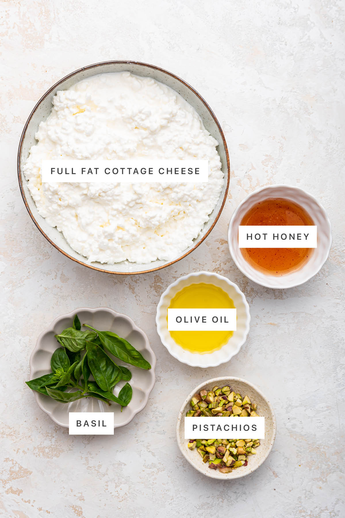 Ingredients measured out to make Hot Honey Whipped Cottage Cheese: cottage cheese, hot honey, olive oil, basil and pistachios.