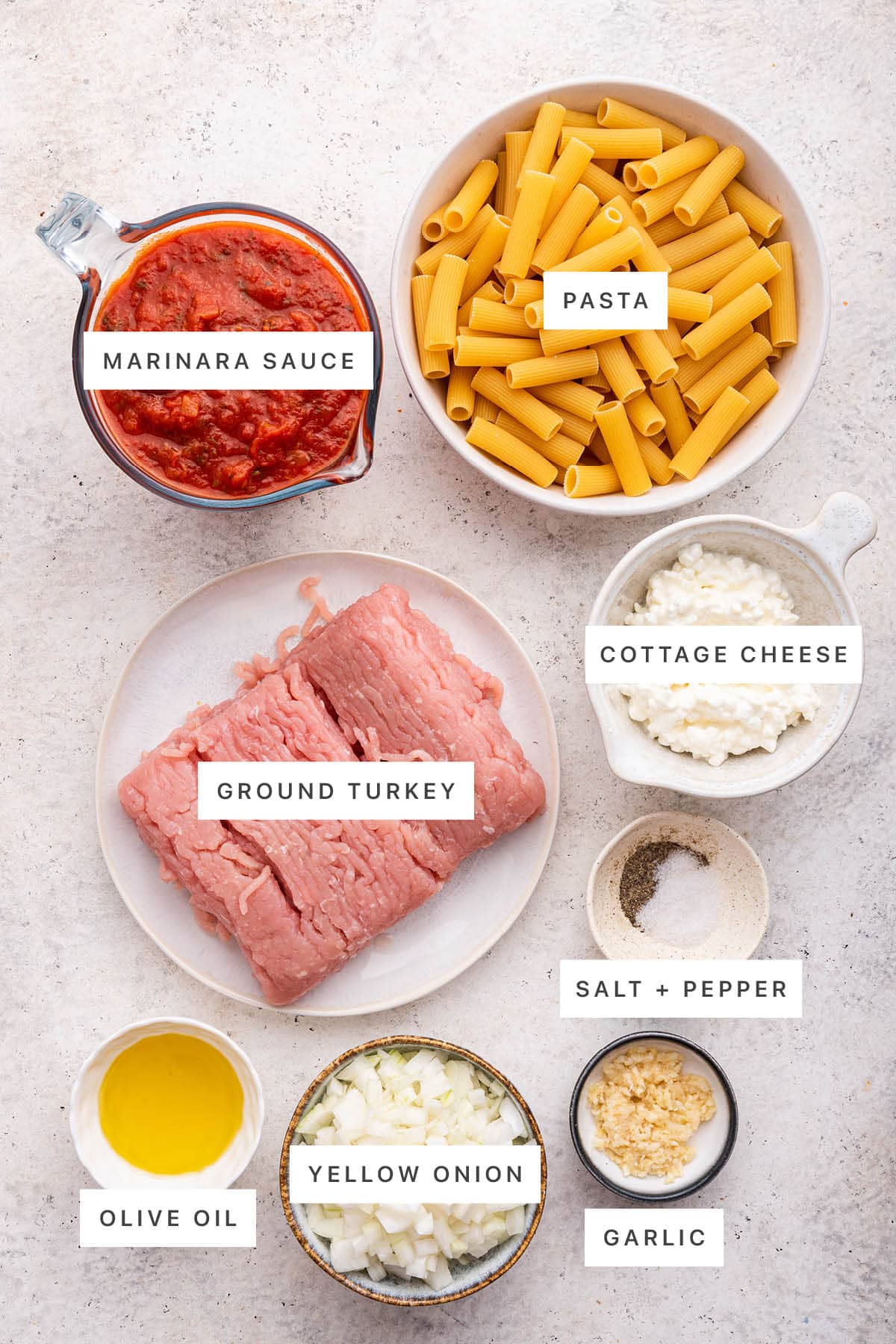 Ingredients measured out to make Creamy Cottage Cheese Pasta: marinara sauce, pasta, ground turkey, cottage cheese, salt, pepper, olive oil, yellow onion and garlic.