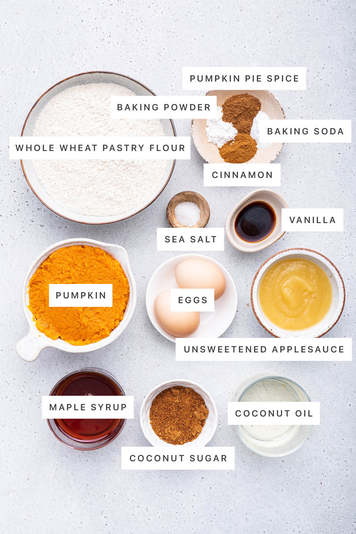 Ingredients measured out to make Healthy Pumpkin Bread: whole wheat pastry flour, baking powder, pumpkin pie spice, baking soda, cinnamon, sea salt, vanilla, pumpkin, eggs, unsweetened applesauce, maple syrup, coconut sugar and coconut oil.