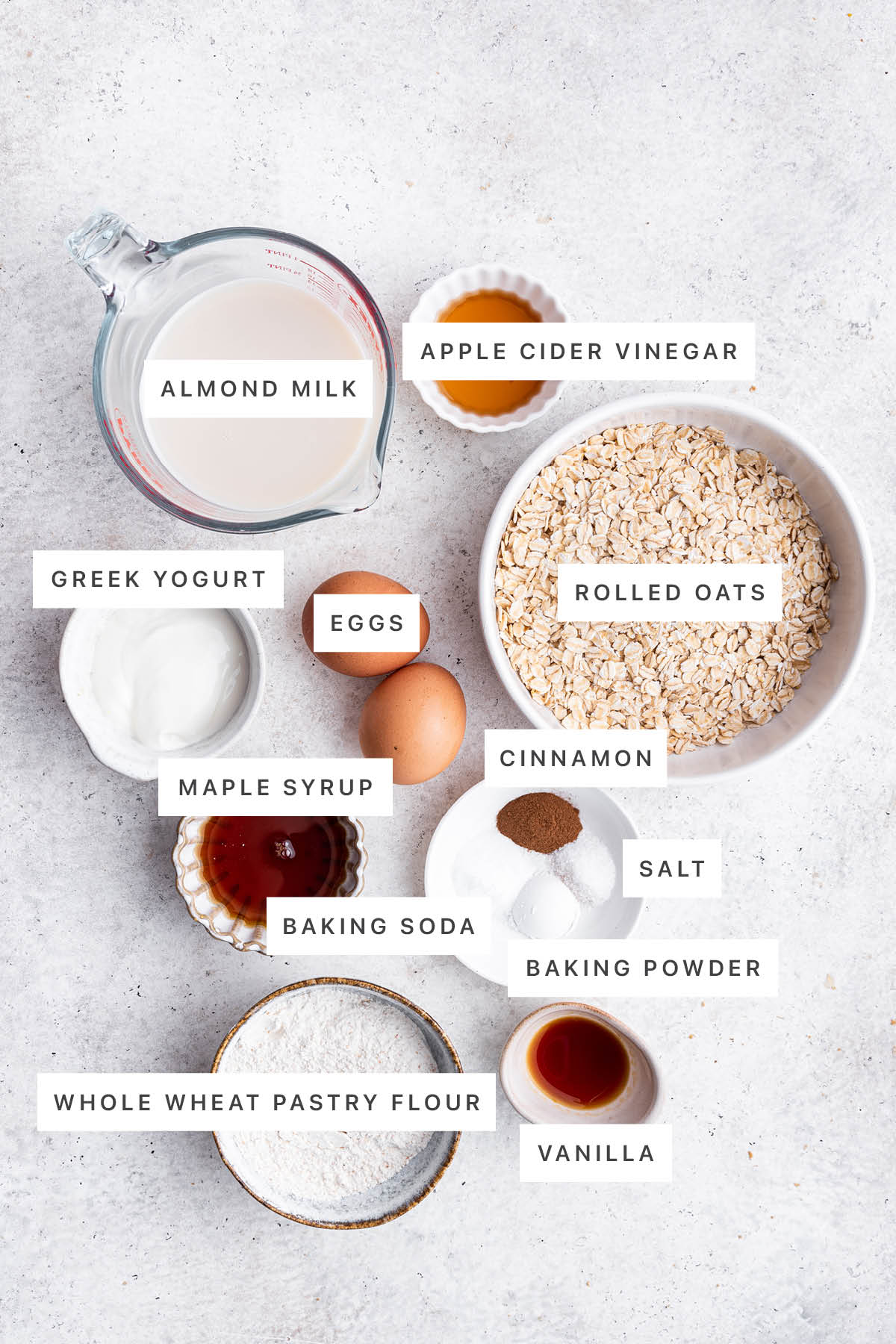 Ingredients measured out to make Overnight Oatmeal Pancakes: almond milk, apple cider vinegar, Greek yogurt, eggs, rolled oats, maple syrup, cinnamon, salt, baking soda, baking powder, whole wheat pastry flour and vanilla.
