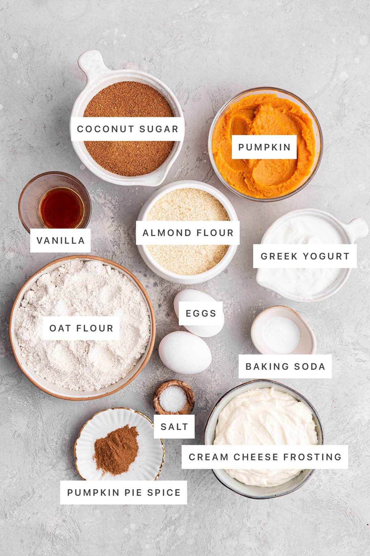 Ingredients measured out to make Healthy Pumpkin Cake: coconut sugar, pumpkin, vanilla, almond flour, Greek yogurt, oat flour, eggs, baking soda, salt, pumpkin pie spice and cream cheese frosting.