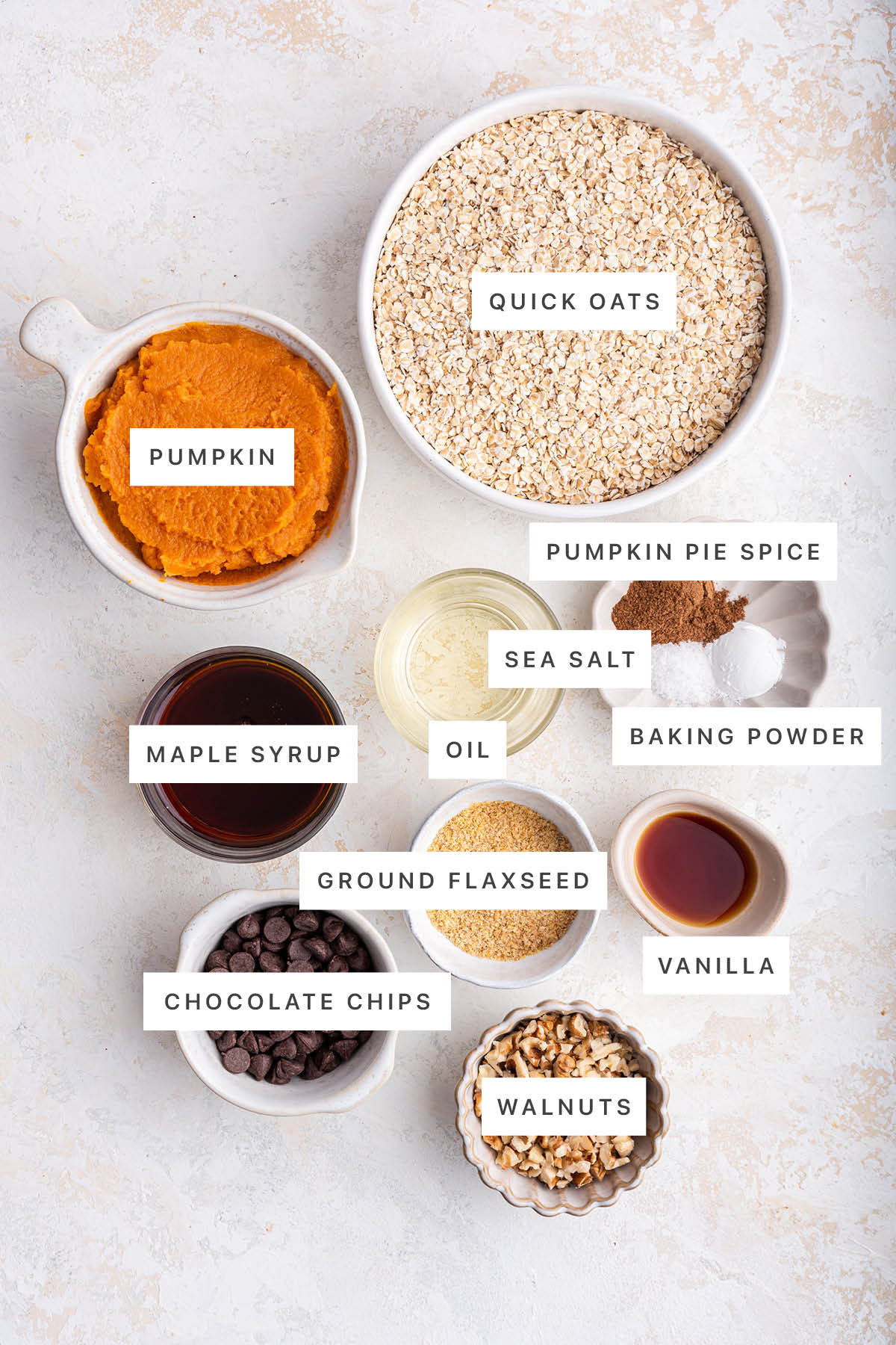 Ingredients measured out to make Pumpkin Oatmeal Bars: pumpkin, quick oats, pumpkin pie spice, sea salt, oil, baking powder, maple syrup, ground flaxseed, vanilla, chocolate chips and walnuts.