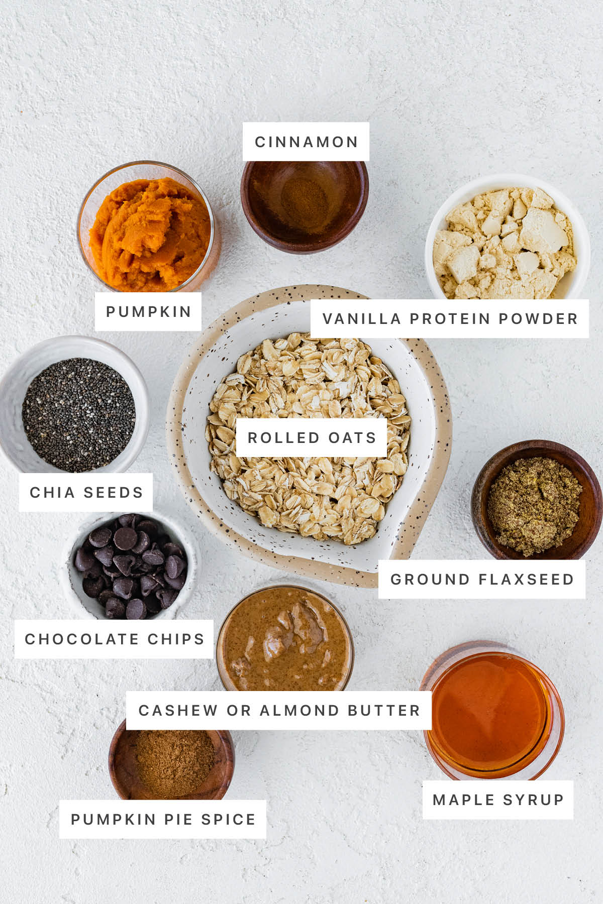 Ingredients measured out to make Pumpkin Protein Balls: pumpkin, cinnamon, vanilla protein powder, chia seeds, rolled oats, ground flaxseed, chocolate chips, almond butter, pumpkin pie spice and maple syrup.