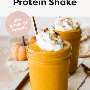 Pumpkin Protein Shake in two glass jars, served with whipped cream, spice and a straw.