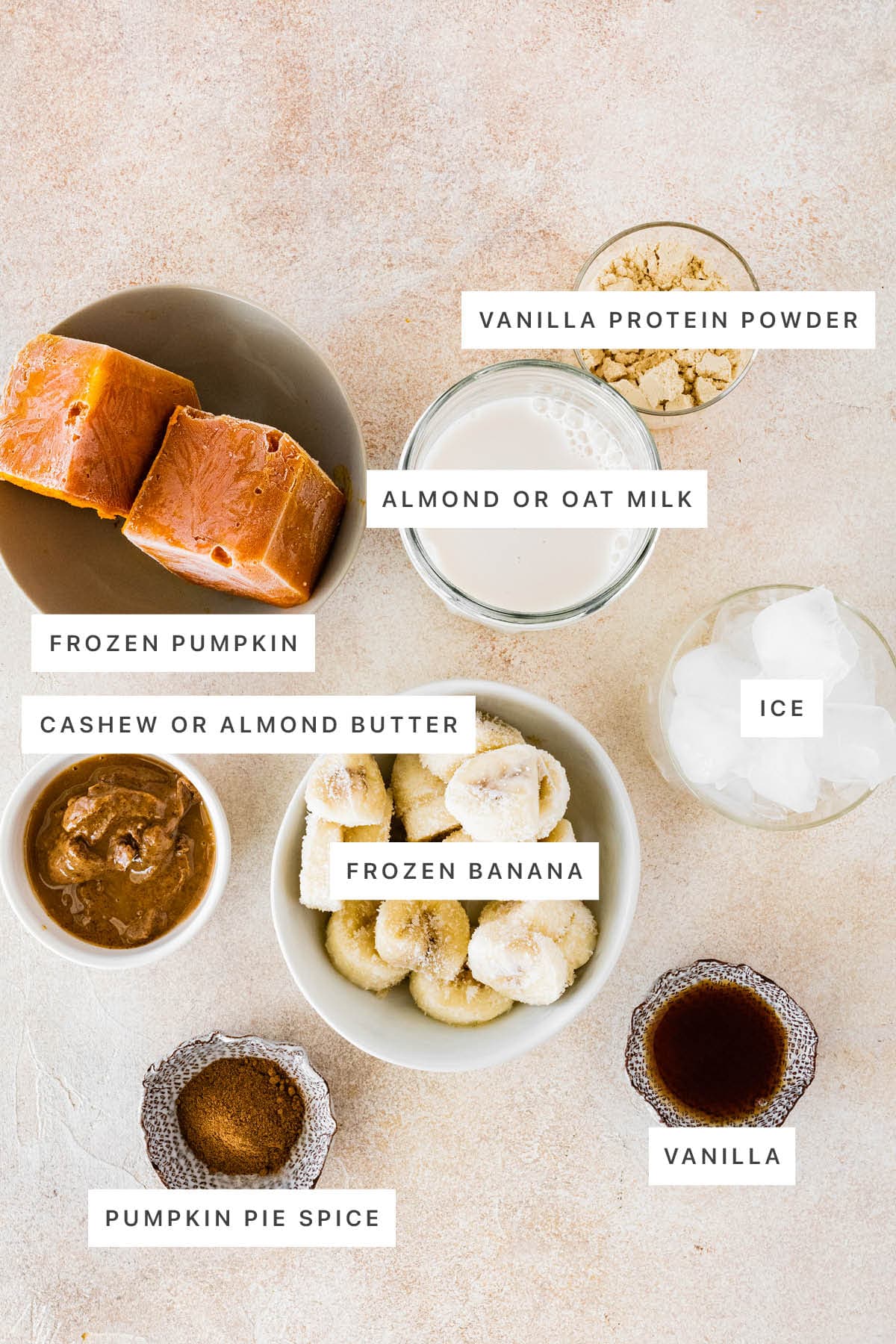 Ingredients measured out to make Pumpkin Protein Shake: frozen pumpkin, almond or oat milk, vanilla protein powder, cashew or almond butter, ice, frozen banana, pumpkin pie spice and vanilla.