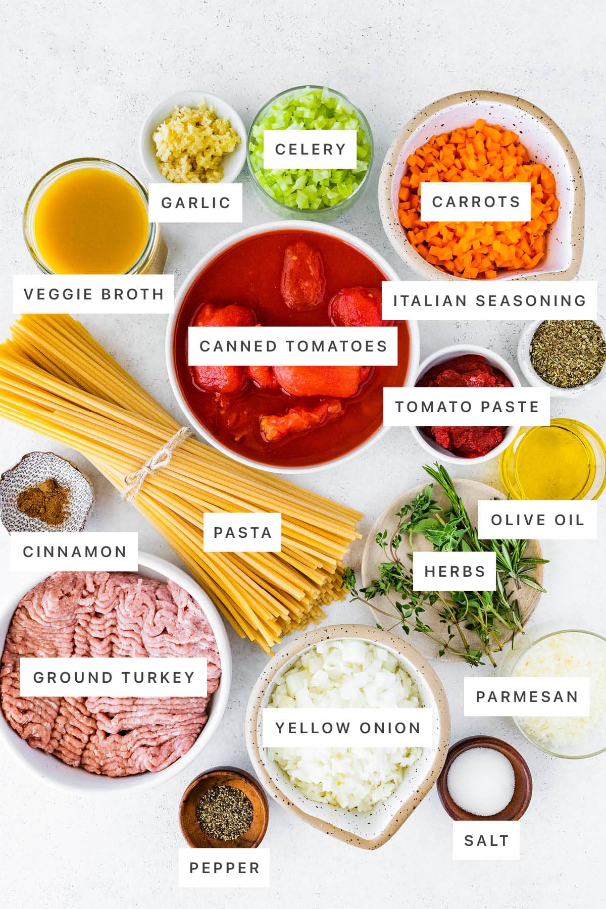 Ingredients measured out to make Turkey Bolognese: veggie broth, garlic, celery, carrots, Italian seasoning, canned tomatoes, tomato paste, cinnamon, pasta, herbs, olive oil, ground turkey, yellow onion, parmesan, salt and pepper.