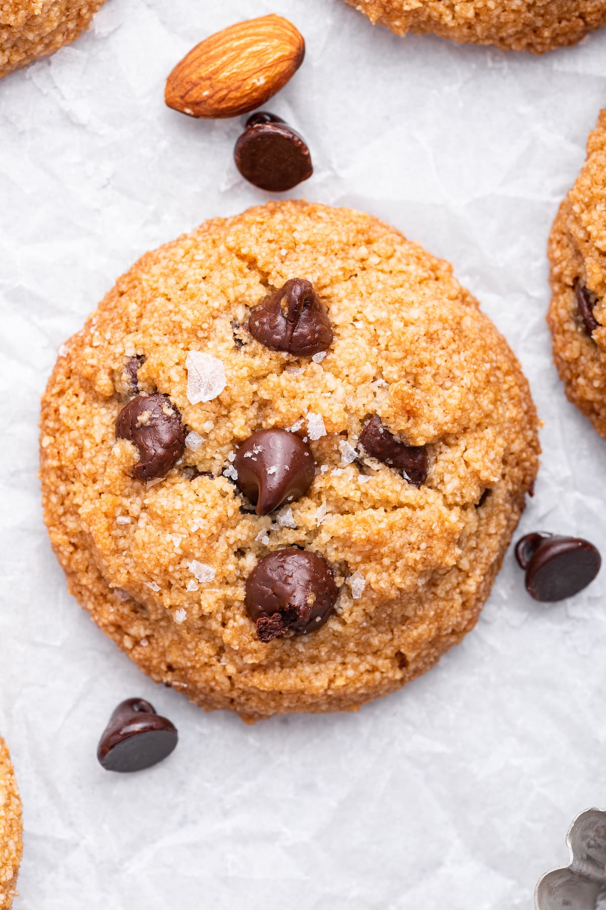 An almond flour chocolate chip cookie with flaky salt on parchment paper.