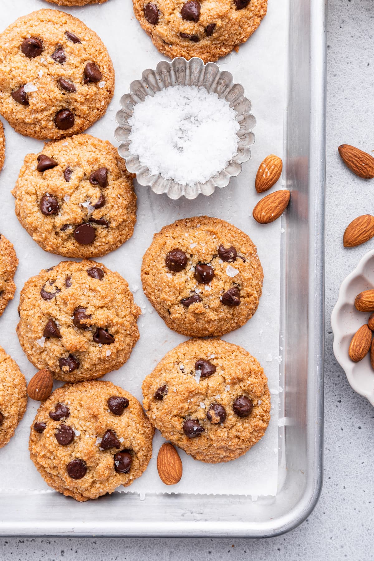 Multiple almond flour chocolate chip cookies on parchment paper on a baking tray.