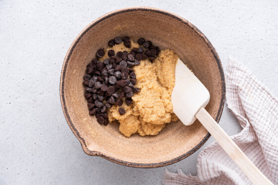 Chocolate chips being added to a large mixing bowl that contains the batter for the almond flour chocolate chip cookies.