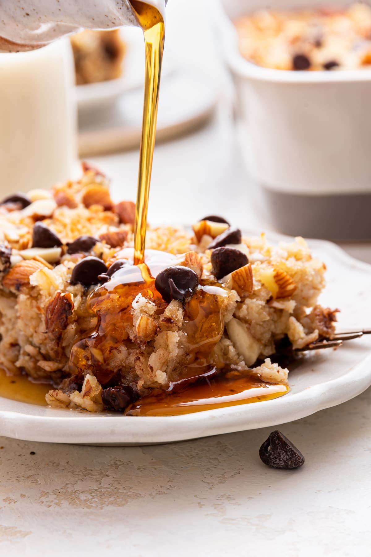 Maple syrup being poured over a serving of almond joy baked oatmeal on a small plate.