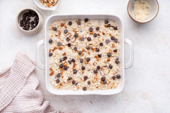 Almond joy baked oatmeal in a square baking dish before being baked and topped with chocolate chips and crushed almonds.