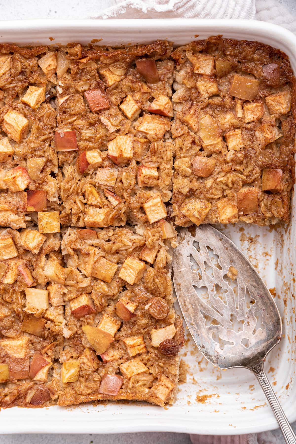 Apple cinnamon baked oatmeal in a square baking dish with a serving spatula and a piece missing.