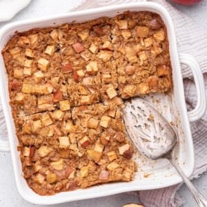 Apple cinnamon baked oatmeal in a square baking dish with a serving spatula and a piece missing.