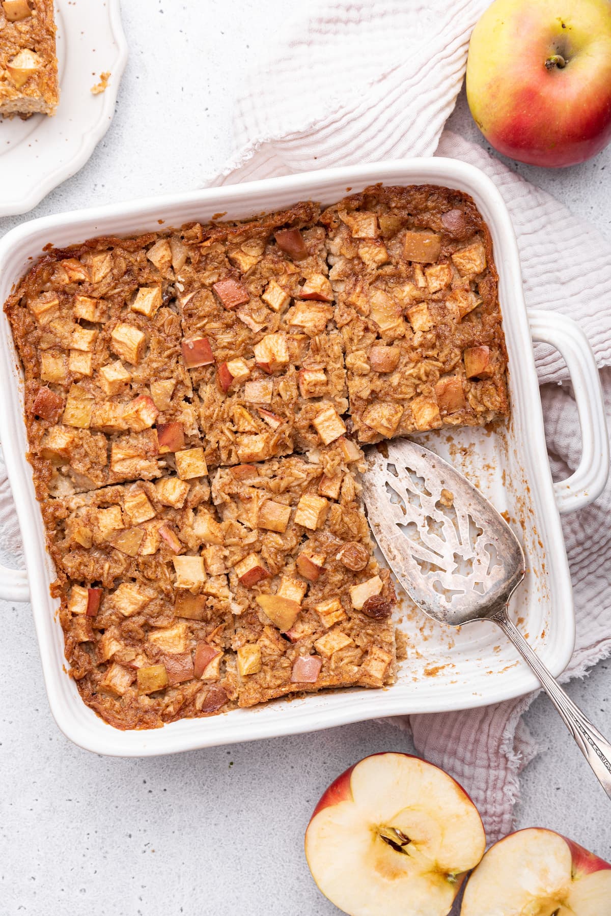 Apple cinnamon baked oatmeal in a square baking dish with a serving spatula and a piece missing.