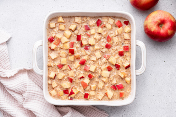 Apple cinnamon baked oatmeal in a square baking dish before being baked and topped with diced apples.