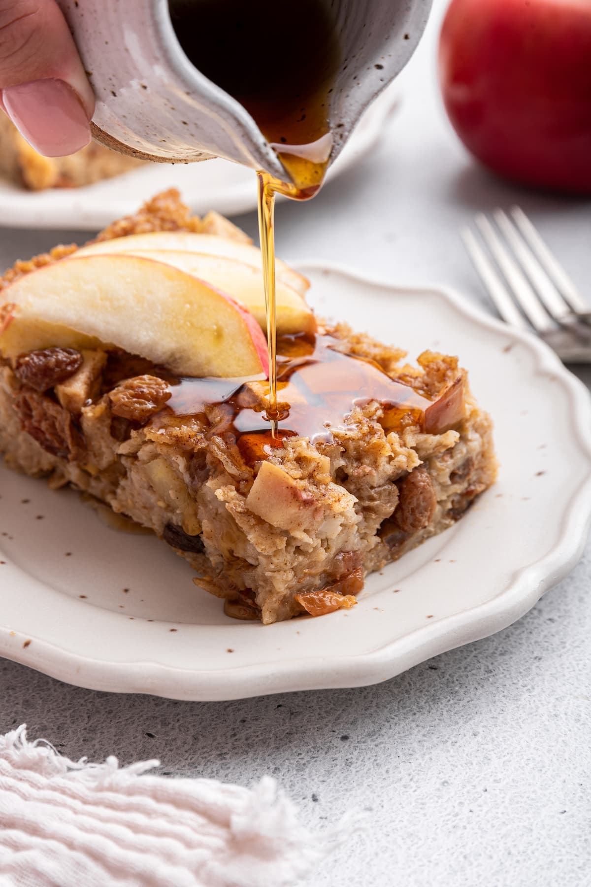 Maple syrup being poured on a piece of apple cinnamon baked oatmeal on a small plate.