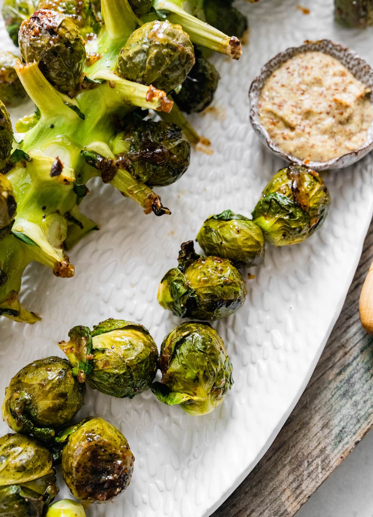 Roasted brussels sprouts on a plate near a small bowl of mustard.
