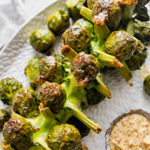 Roasted Brussels Sprouts on the Stalk on a large serving plate near a small bowl of mustard.