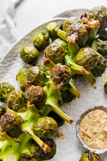 Roasted Brussels Sprouts on the Stalk on a large serving plate near a small bowl of mustard.