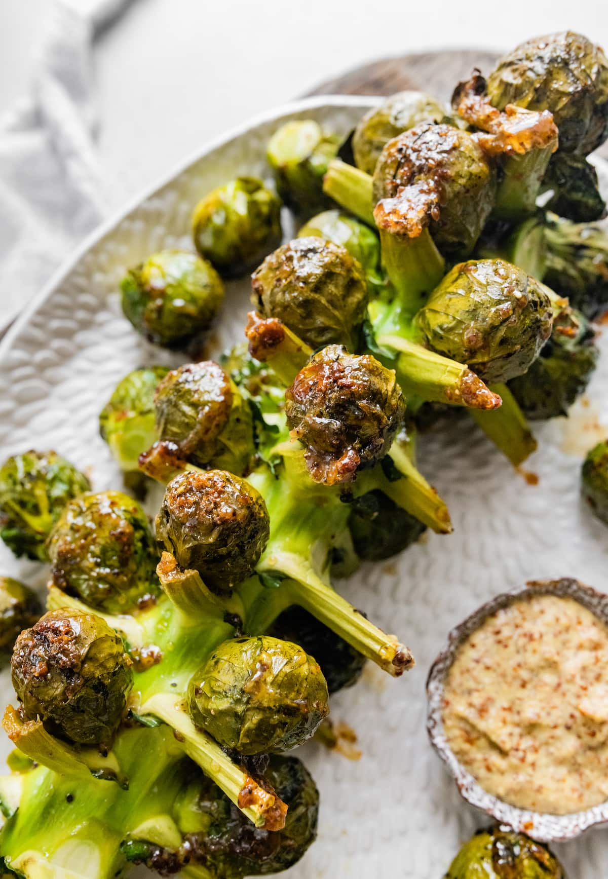Roasted Brussels Sprouts on the Stalk on a large serving plate near a small bowl of mustard.