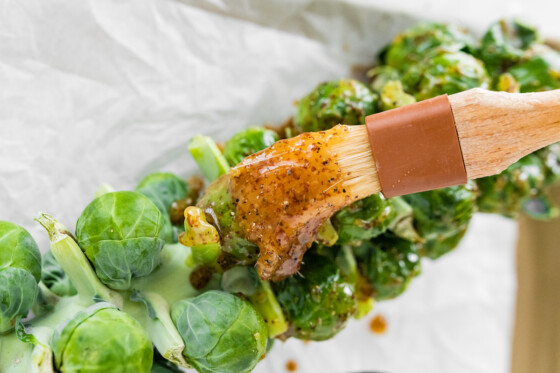 A small brush glazing a mustard sauce on Brussels Sprouts on the Stalk.