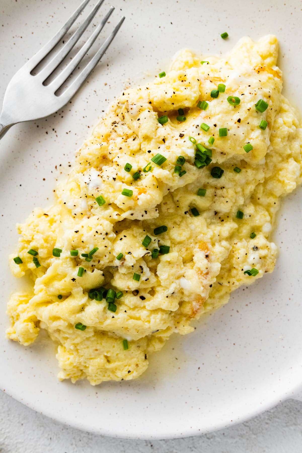 Cottage cheese scrambled eggs on a plate garnished with fresh chives, salt, and pepper.