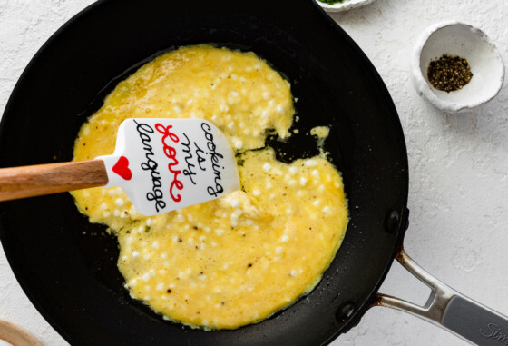 A silicone spatula being used to scramble eggs and cottage cheese in a skillet.
