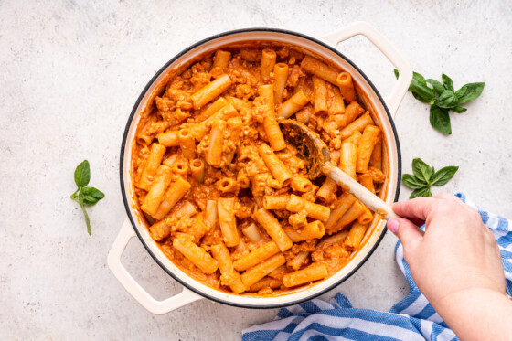 Pasta mixed with the turkey, and marinara and cottage cheese sauce in a large dutch oven with a woman's hand using a wooden spoon to mix it.