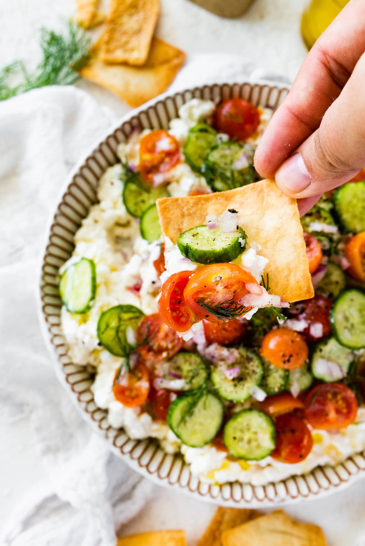 A hand holding a pita chip with some cottage cheese salad on it.