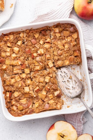 Apple cinnamon baked oatmeal in a square baking dish with a serving spatula and a piece missing.