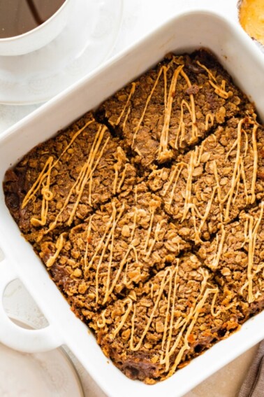 Coffee baked oatmeal sliced in a square baking dish and topped with a drizzle of nut butter.