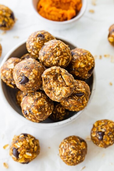 Many pumpkin protein balls in a small bowl with one of them having a bite taken from it.