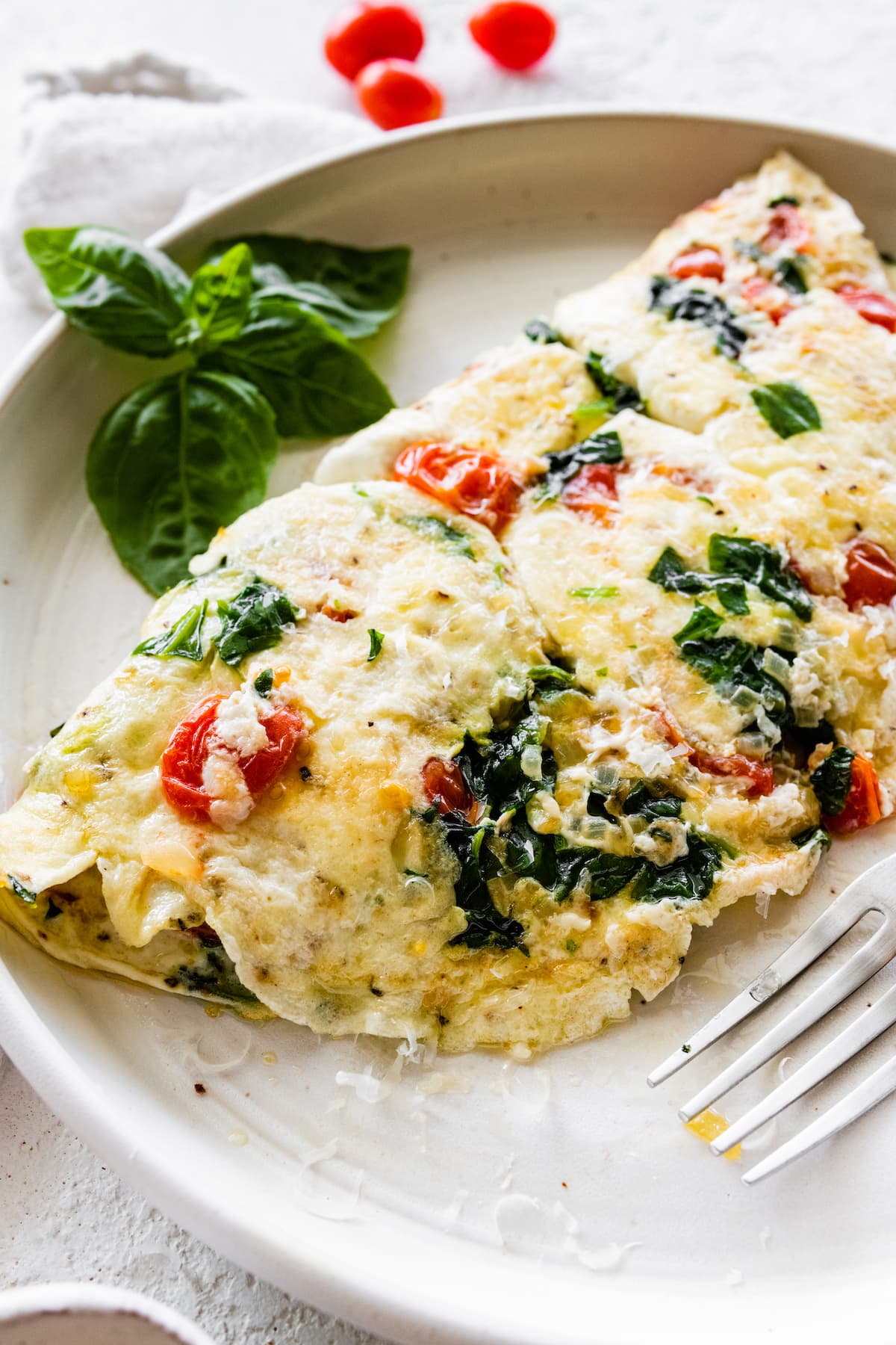 Close up of an egg white omelette on a plate served with a fork and fresh basil.