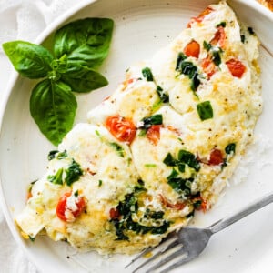 An egg white omelette on a plate served with a fork and fresh basil.
