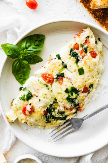 An egg white omelette on a plate served with a fork and fresh basil.