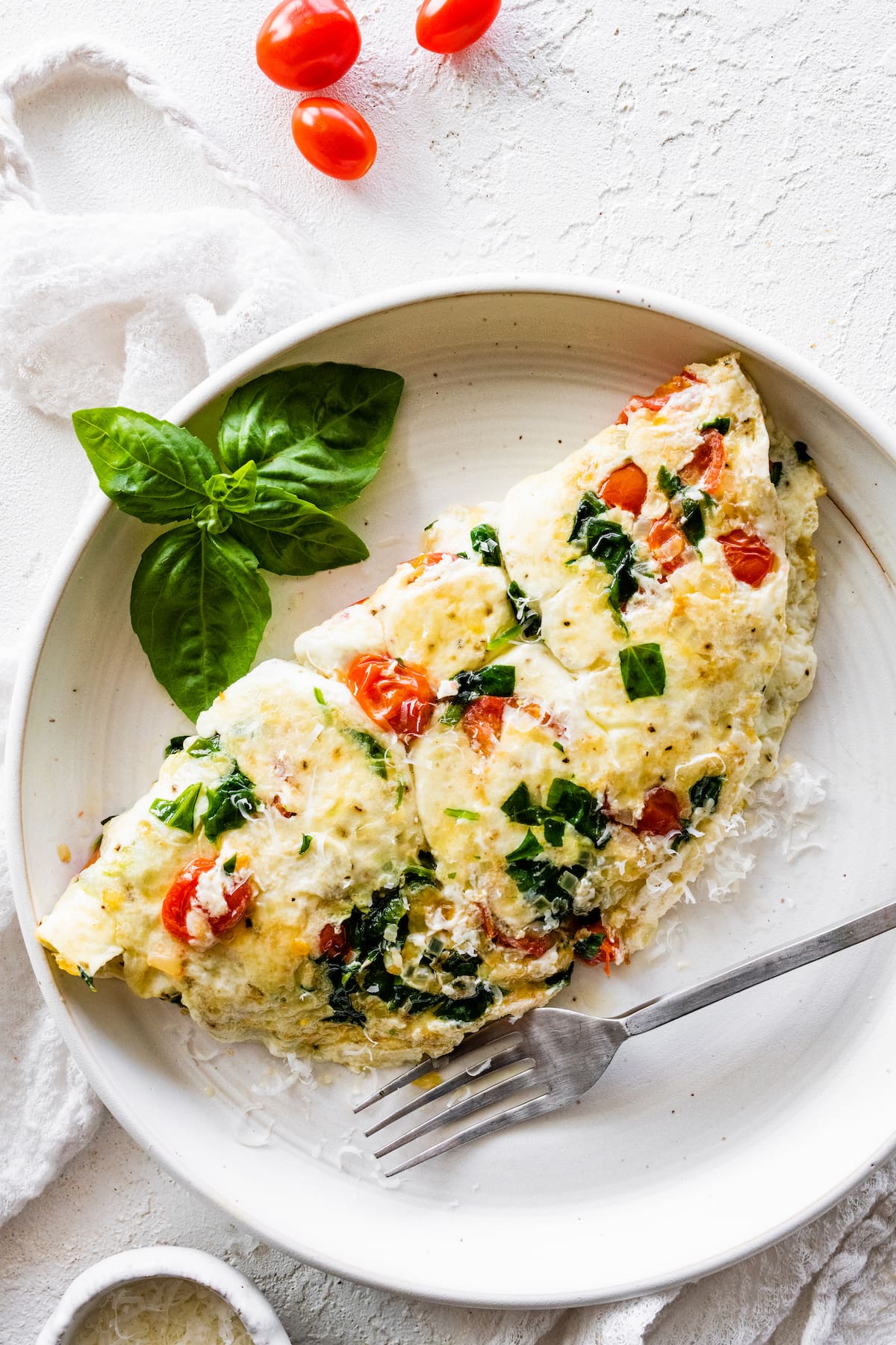 An egg white omelette on a plate served with a fork and fresh basil.