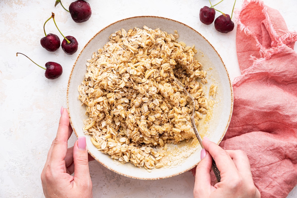 A woman's hand uses a fork to mix oats and flour to create a crisp.
