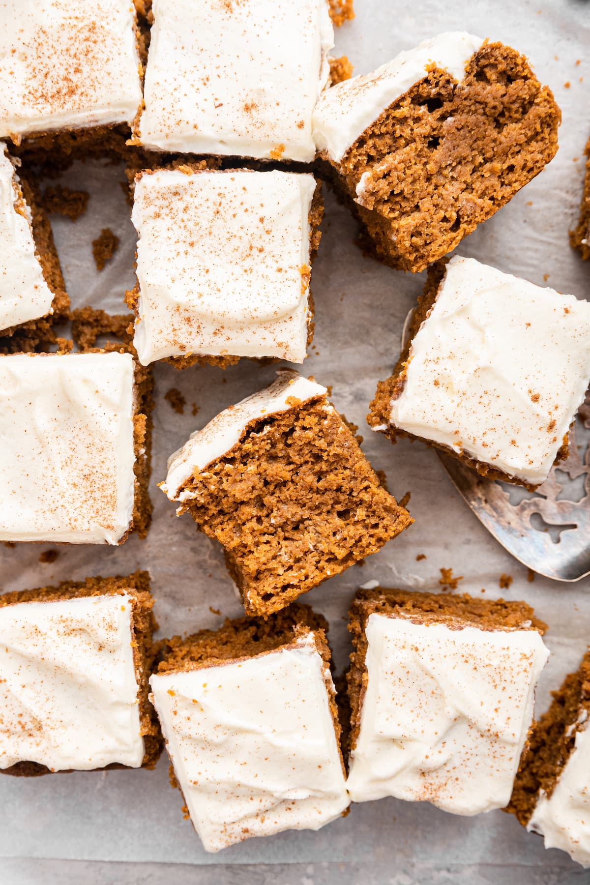 Pumpkin cake slices with a cream cheese frosting on parchment paper.