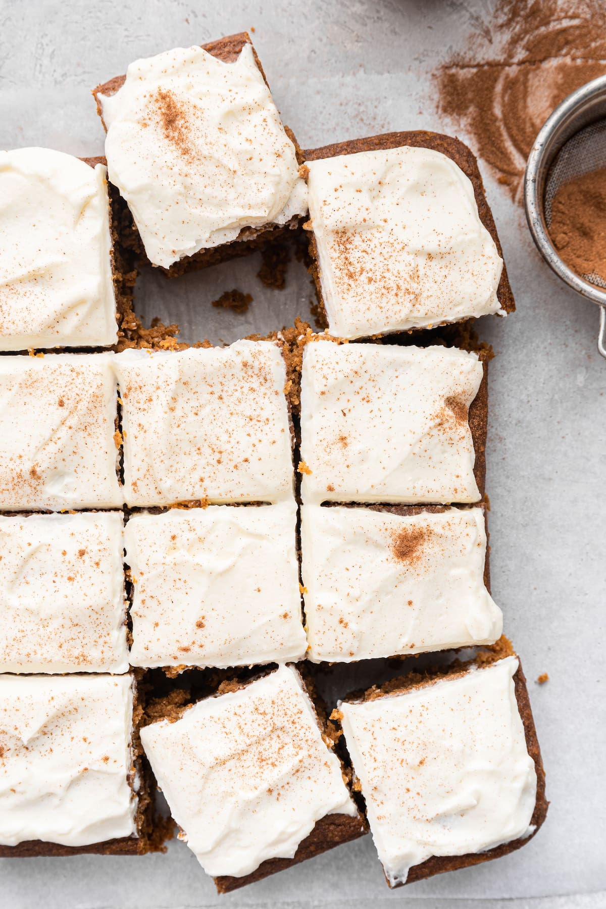 Pumpkin cake slices with a cream cheese frosting on parchment paper.