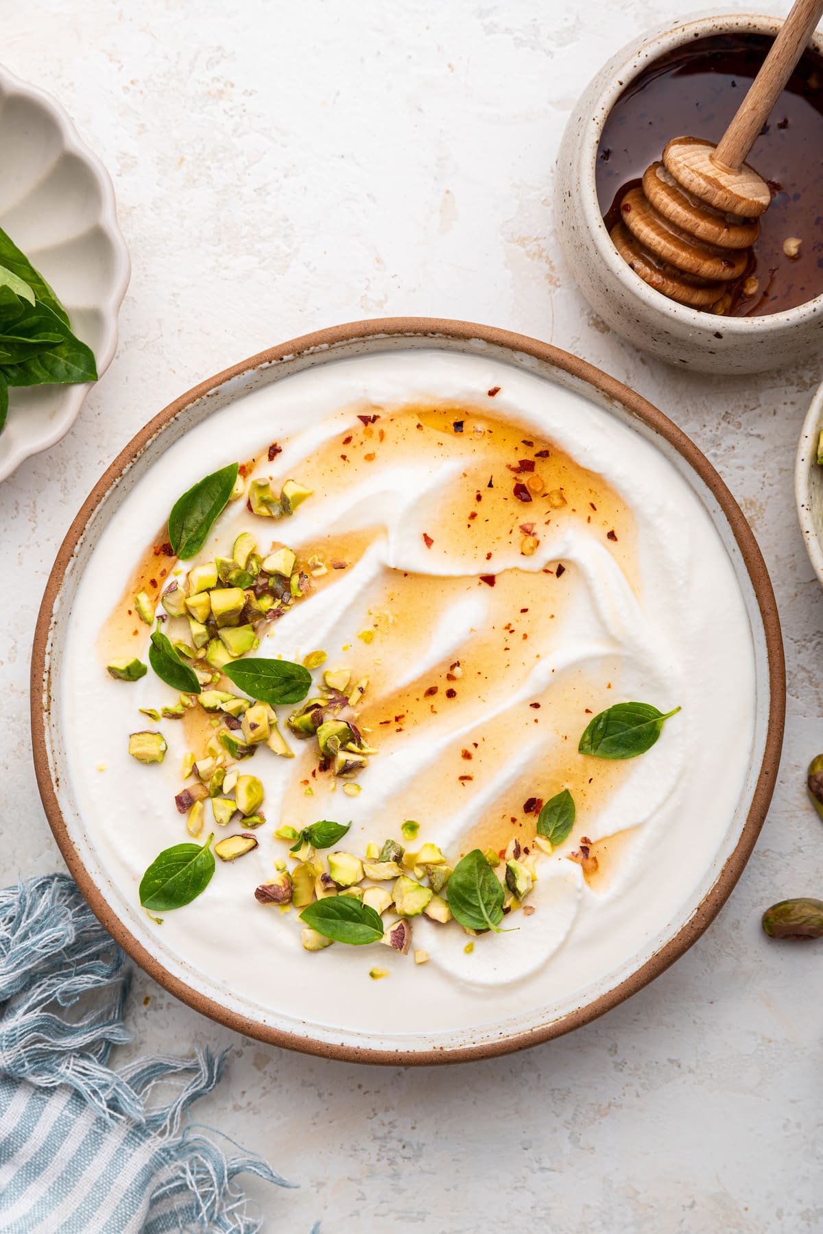 Hot honey whipped cottage cheese in a shallow bowl topped with with a drizzle of hot honey, olive oil, crack of black pepper, fresh basil and chopped pistachios.