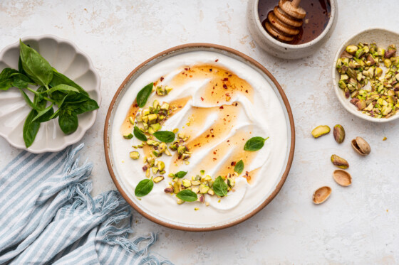 Hot honey whipped cottage cheese in a shallow bowl topped with with a drizzle of hot honey, olive oil, crack of black pepper, fresh basil and chopped pistachios.