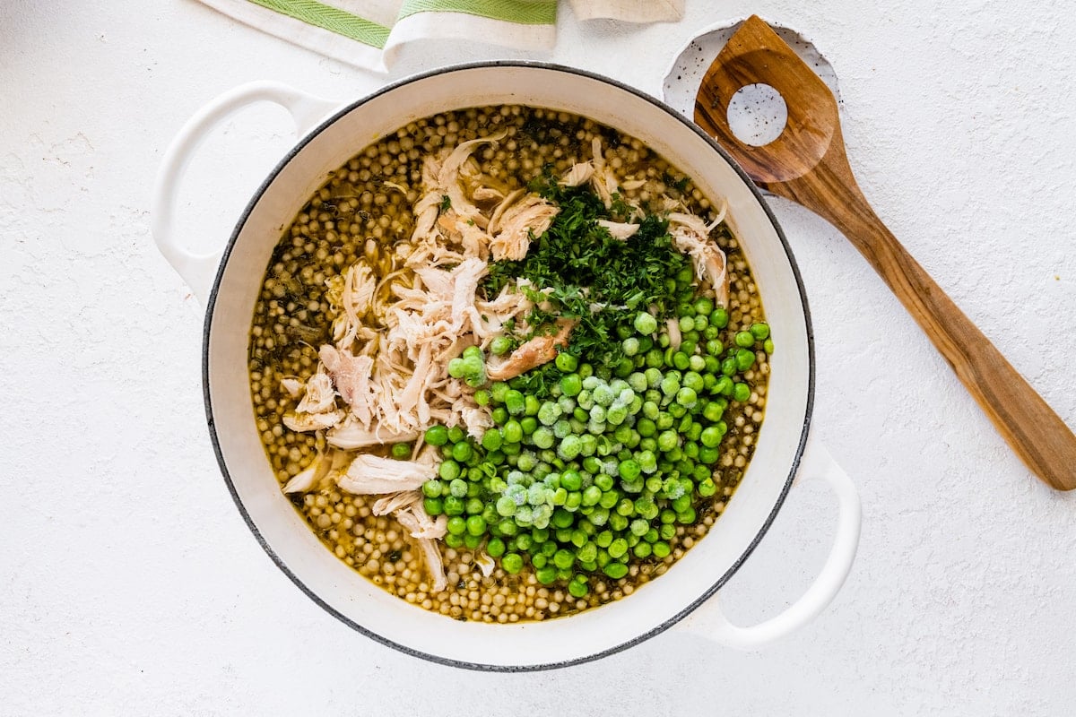 Turkey, greens, and frozen peas added to a large pot of broth for turkey soup.