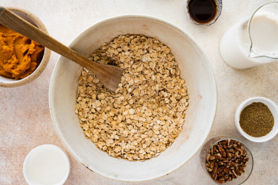 Rolled oats used for the pumpkin baked oatmeal in a large mixing bowl with a wooden spoon.