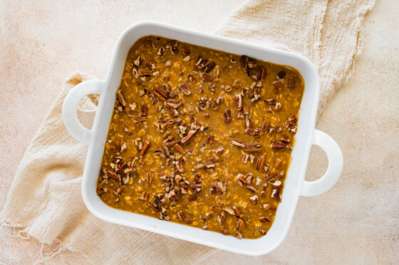 Pumpkin baked oatmeal batter added to a square baking dish and topped with crushed pecans.