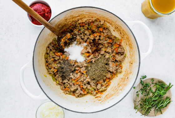 Herbs and spices are added to a large dutch oven containing cooked turkey and vegetables.