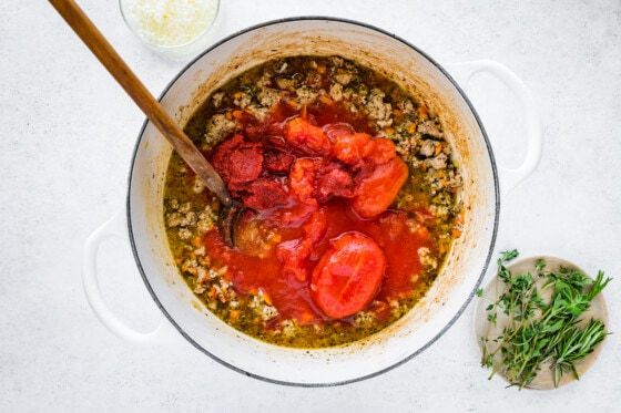 Tomatoes and tomato paste added to a large dutch oven with cooked turkey, vegetables, herbs and spices to create a turkey bolognese.