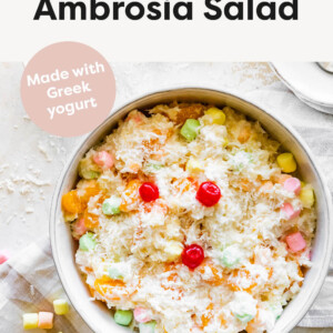 Serving bowl of ambrosia salad topped with coconut and cherries.